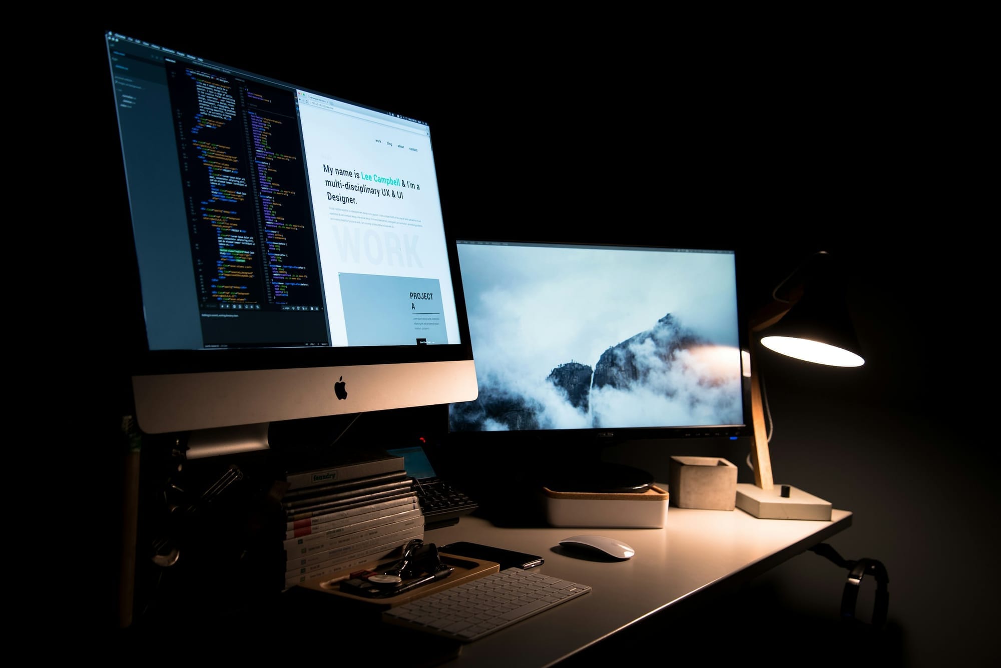 A dark desk with two computer displays showing code and a portfolio website.