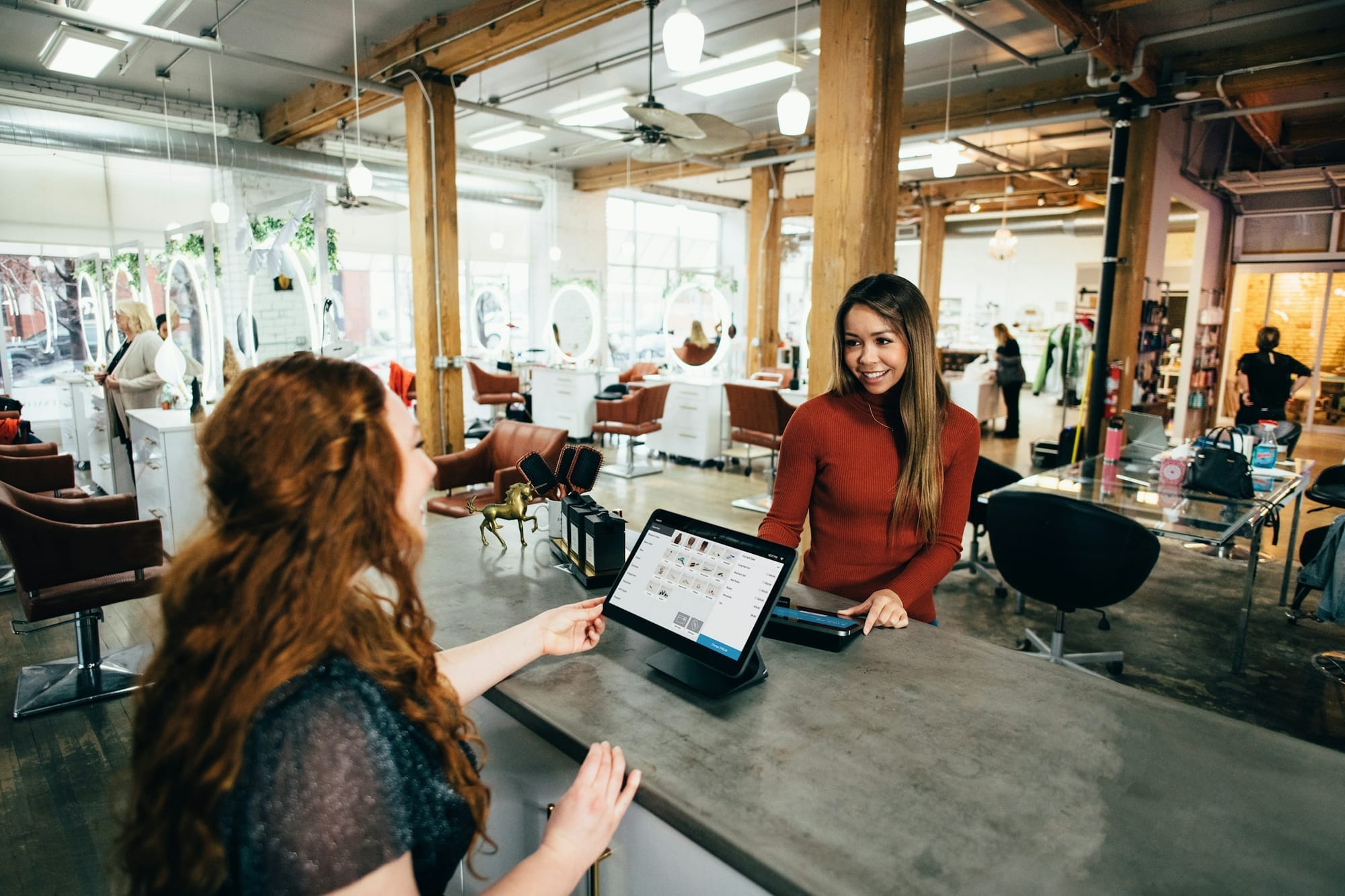 A customer paying at a digital checkout counter in a bright hair salon.
