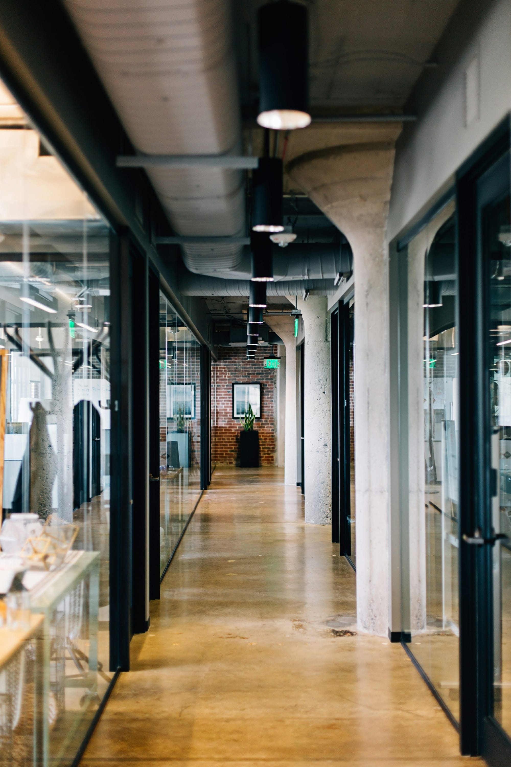 A long glass-walled corridor in a modern industrial-style office.