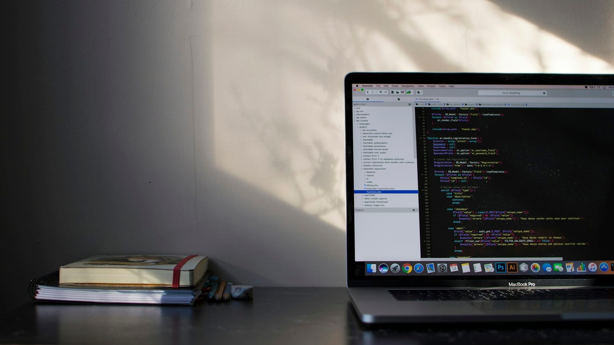 A laptop displaying source code beside notebooks on a sunlit desk.