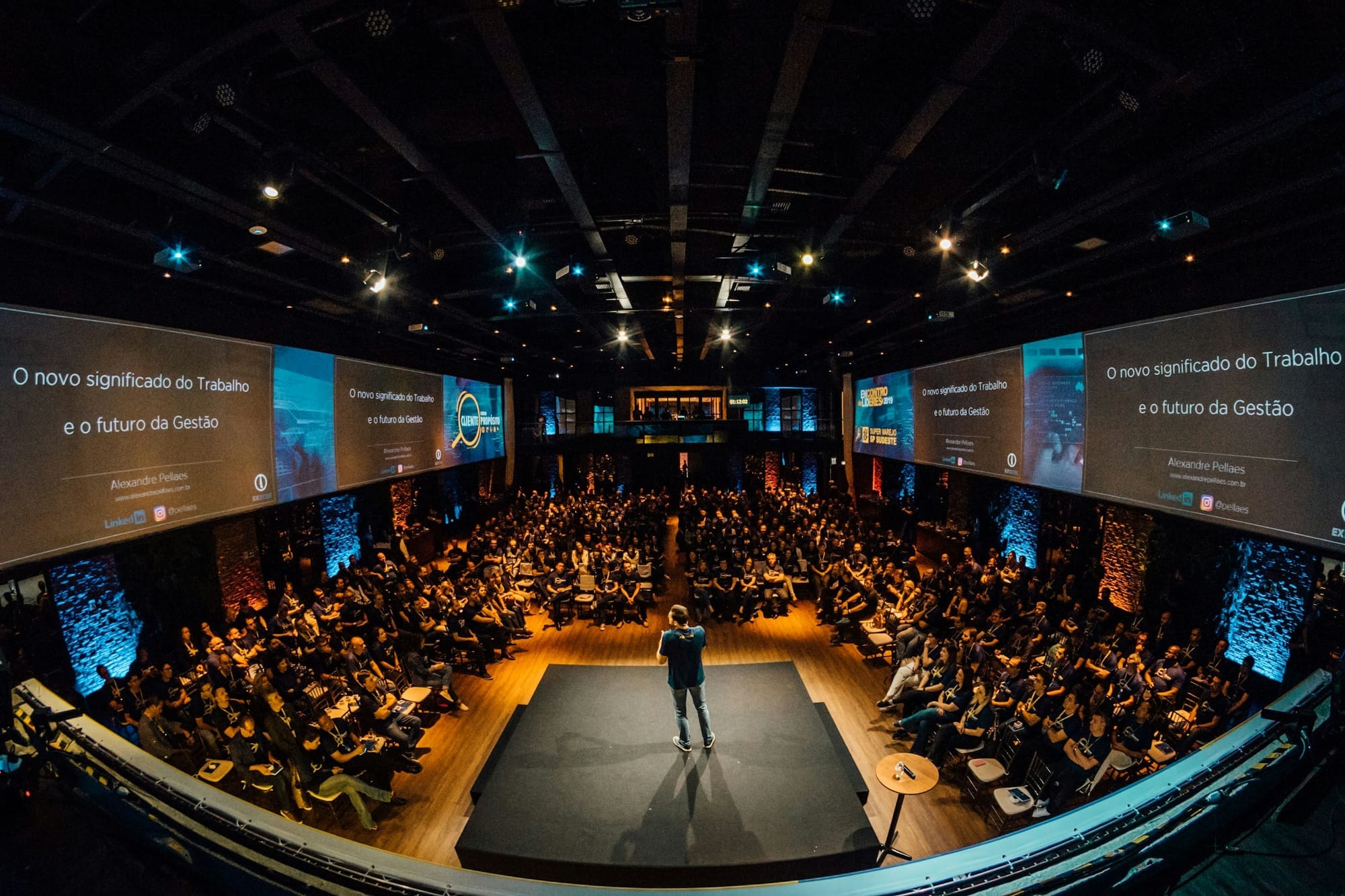 A speaker addressing a large audience in a dark auditorium.
