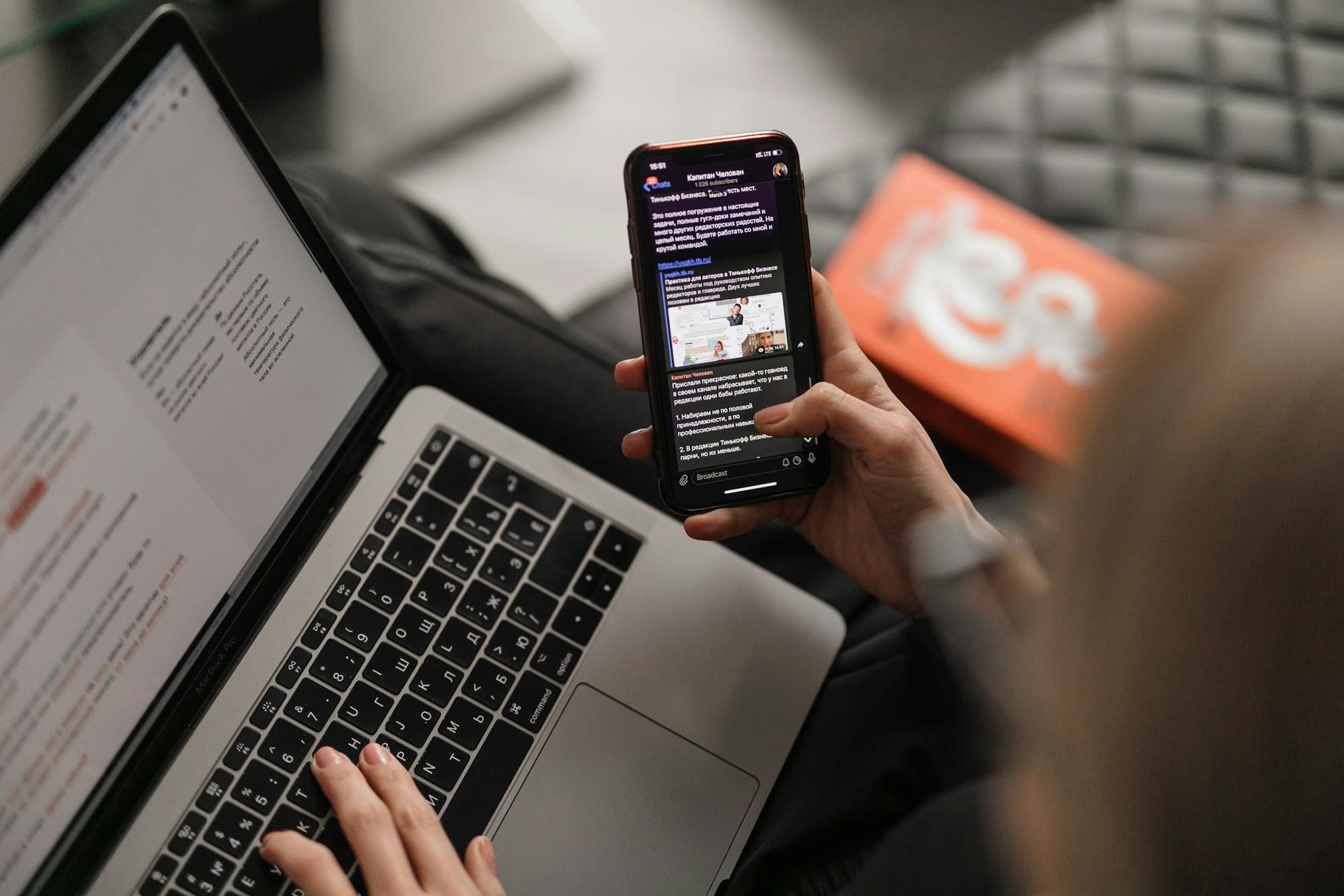 A person reading a broadcast message on a phone beside an open laptop.