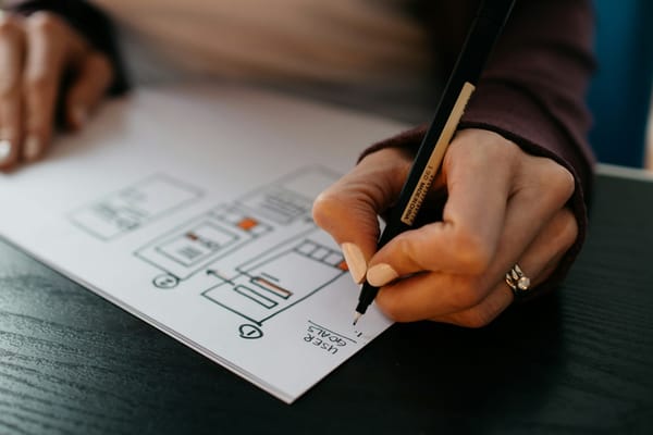 A person sketching interface ideas on paper at a dark table.