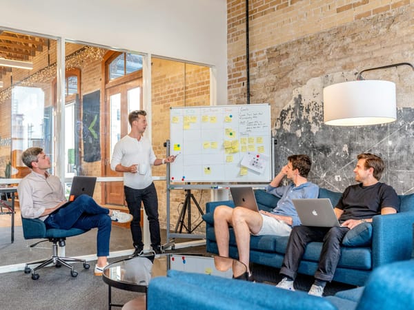 Four colleagues discussing work beside a whiteboard in a brick-walled office.