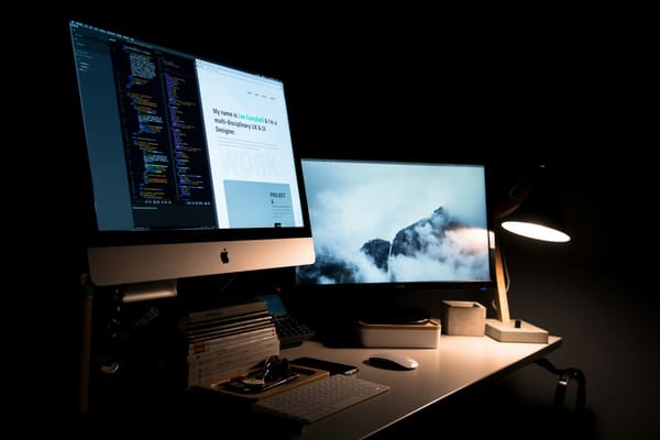 A dark desk with two computer displays showing code and a portfolio website.