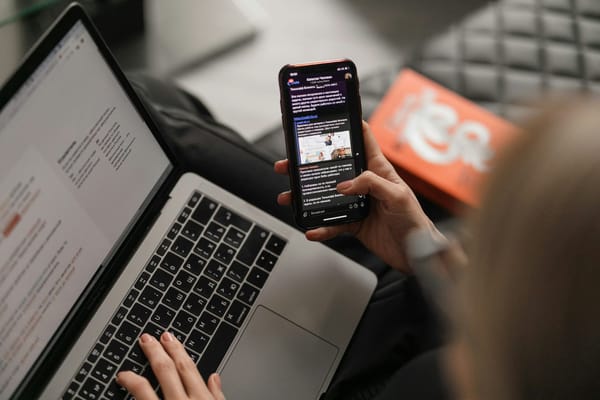 A person reading a broadcast message on a phone beside an open laptop.