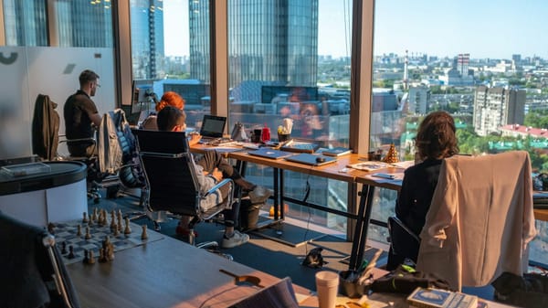 Colleagues working independently in a bright office overlooking a city.