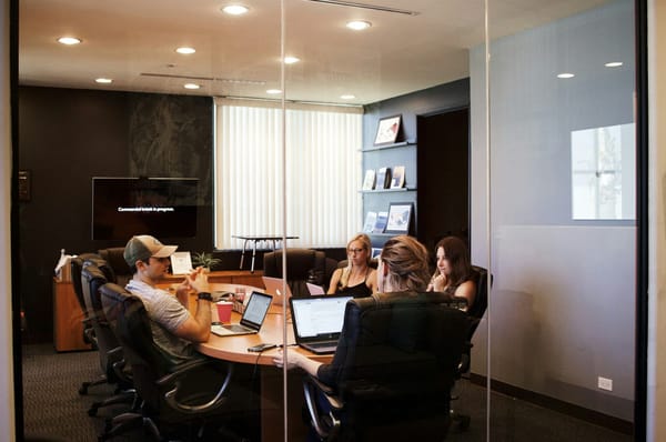 Five colleagues meeting around a conference table behind a glass wall.